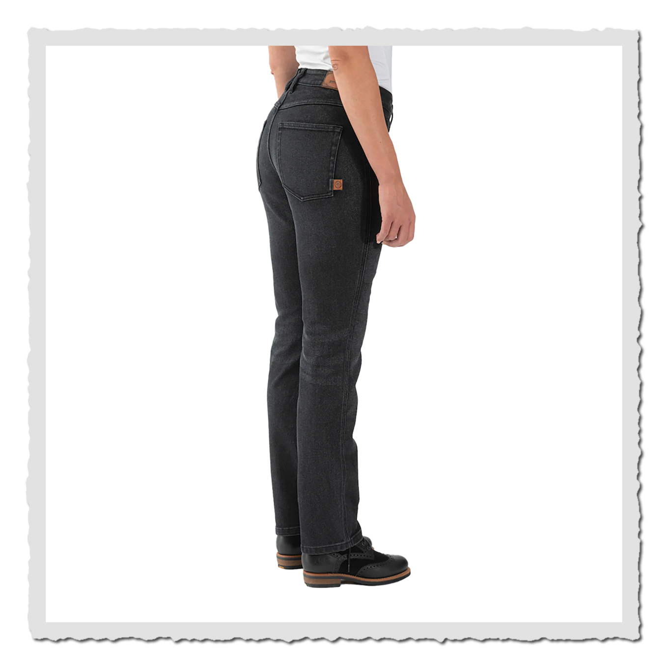 Person in schwarzer Jeans aus seitlicher Rückansicht vor hellem Hintergrund, mit weißem Oberteil und schwarzen Schuhen.